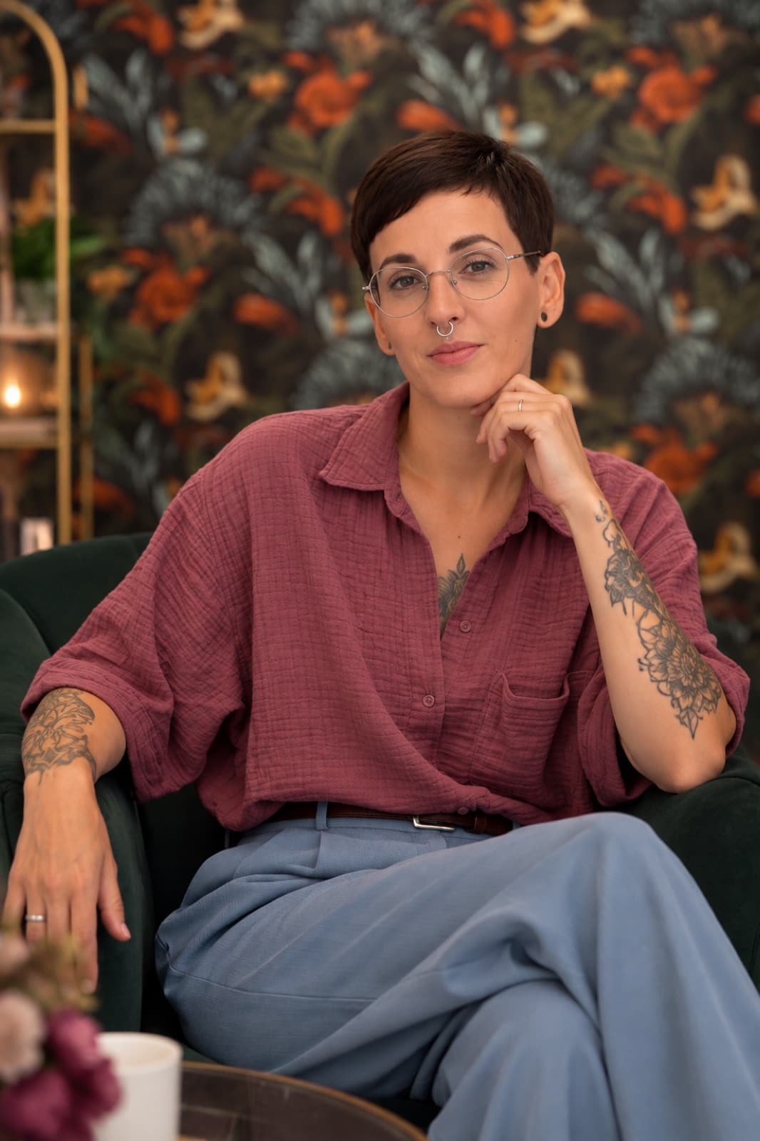 Laura Maskus im Sessel vor einer dunklen Blumentapete, den Kopf auf die Hand gestützt